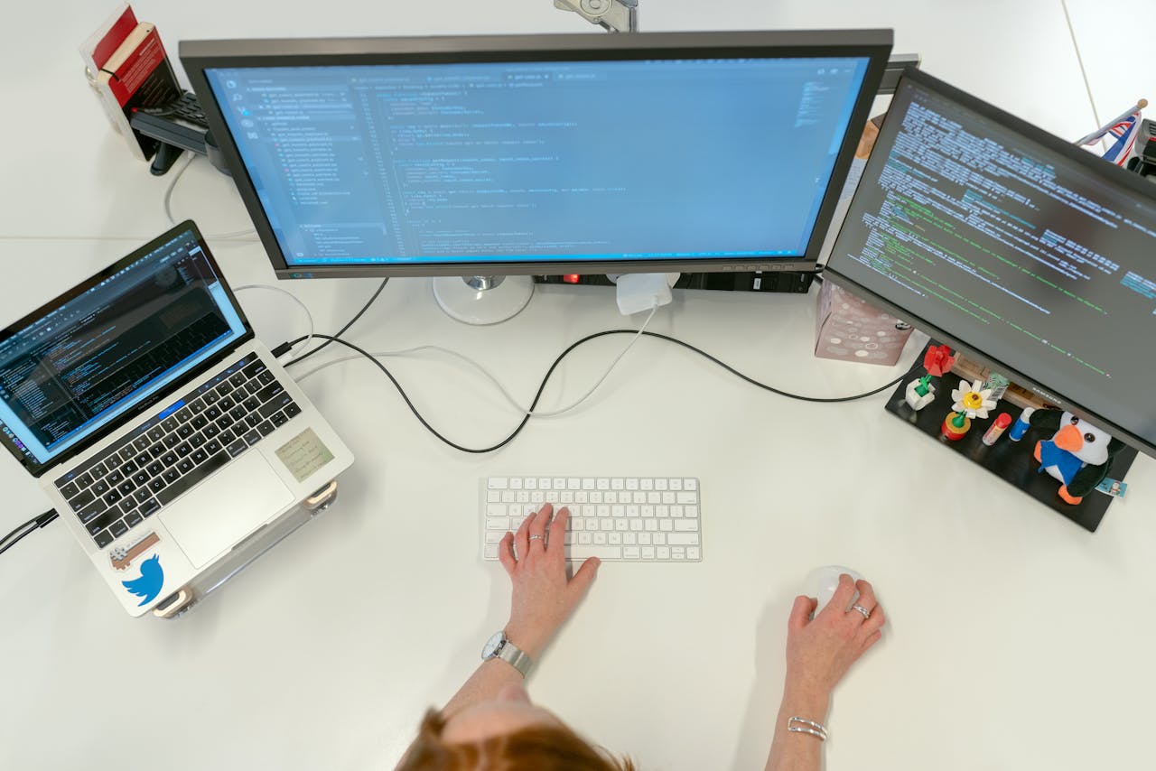 awards-img A female software engineer coding on dual monitors and a laptop in an office setting.