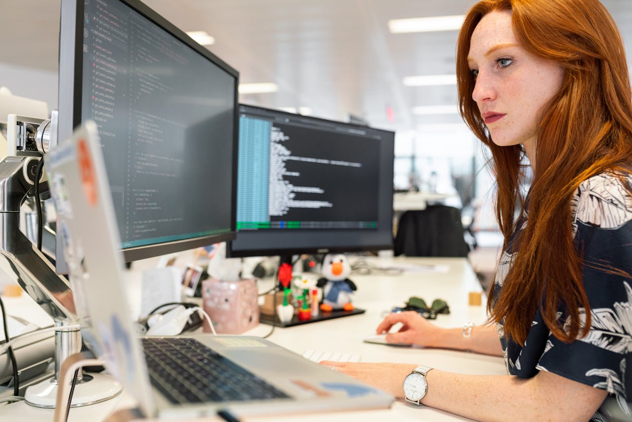 client-satisfaction-img A focused female software engineer coding on dual monitors in a modern office.